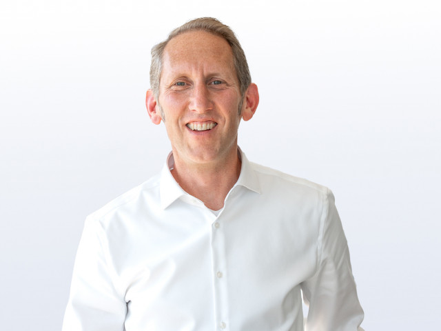 Der l&auml;chelnde Standortleiter von TriFinance in Hamburg, Martin Kunze, l&auml;chelt vor wei&szlig;em Hintergrund in die Kamera.